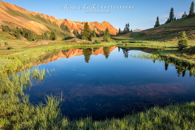 A pond reflects the vibrant colors of the sky and mountain. One of the San Juan Mountain's, Red Mountains is visible.